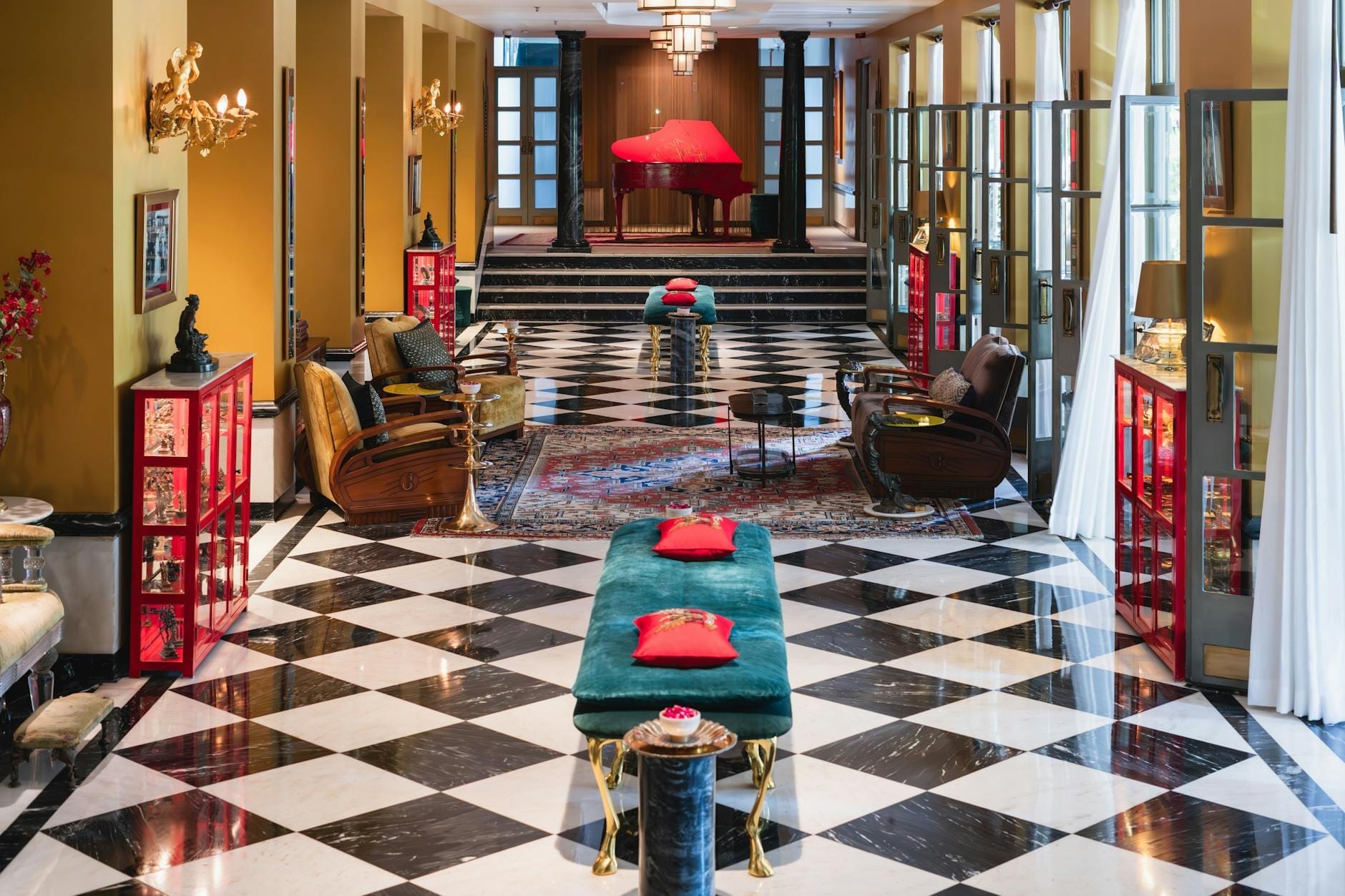 Elegante saguão de hotel em Lisboa com pisos de mármore xadrez preto e branco, assentos de veludo macio, detalhes dourados e um impressionante piano de cauda vermelho.