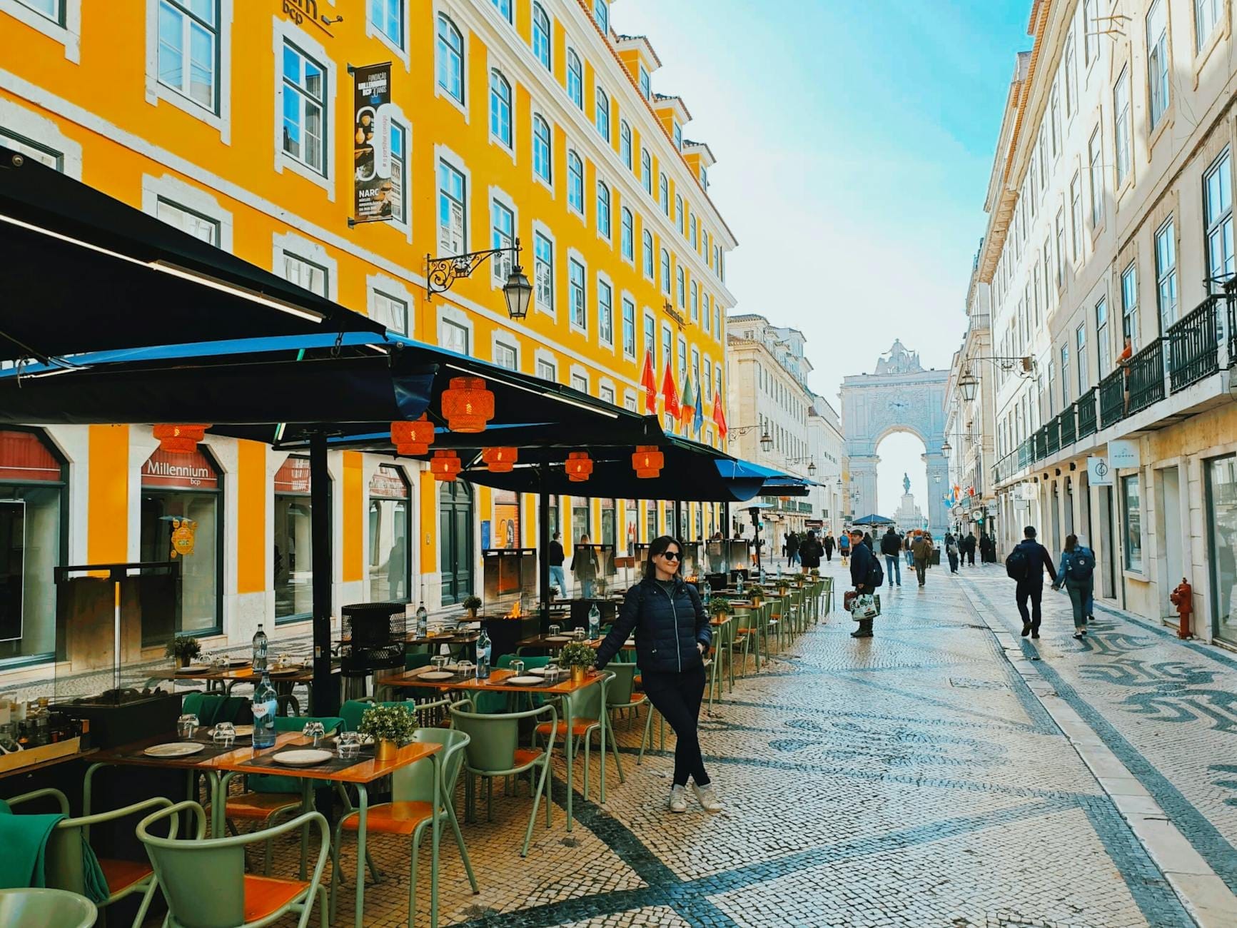 Vista da Rua Augusta na Baixa de Lisboa, com cafés ao ar livre, pedestres e o Arco da Rua Augusta ao fundo.