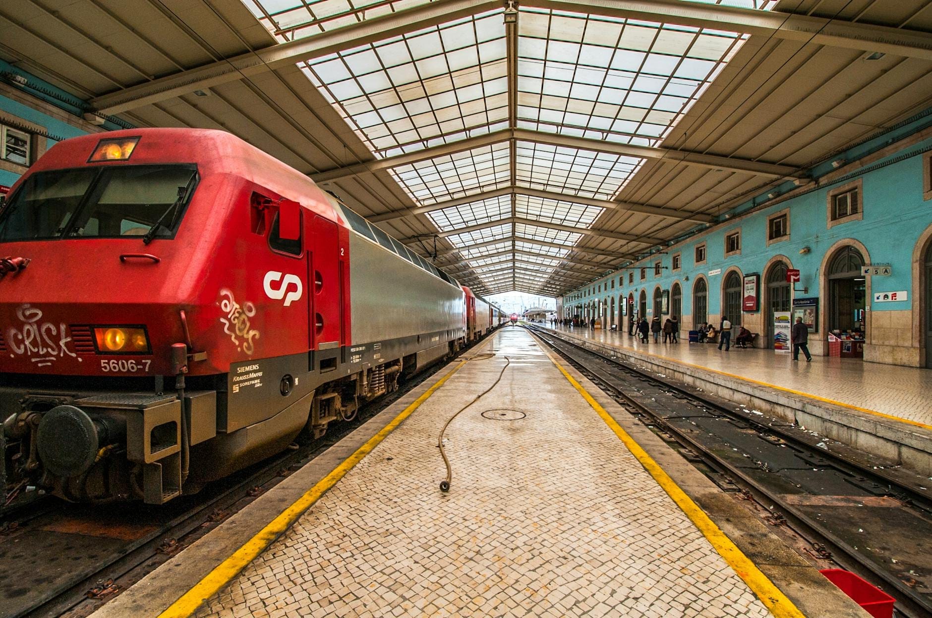 Un train rouge de CP à la gare historique de Lisboa Santa Apolónia, avec ses azulejos bleus, ses entrées en arche et son toit en verre.