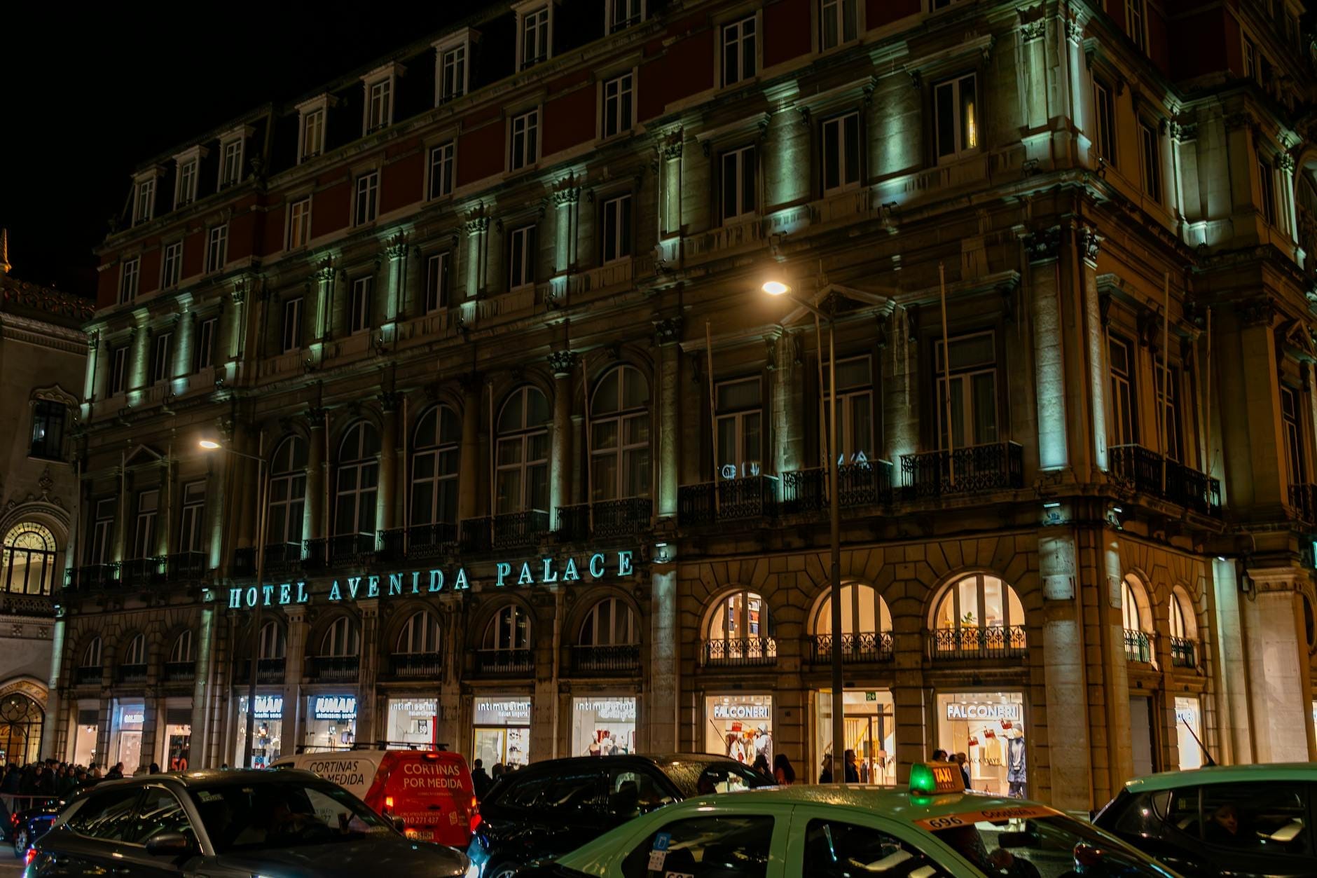 Hôtel Avenida Palace à Lisbonne illuminé la nuit avec des voitures et des personnes devant l'entrée.