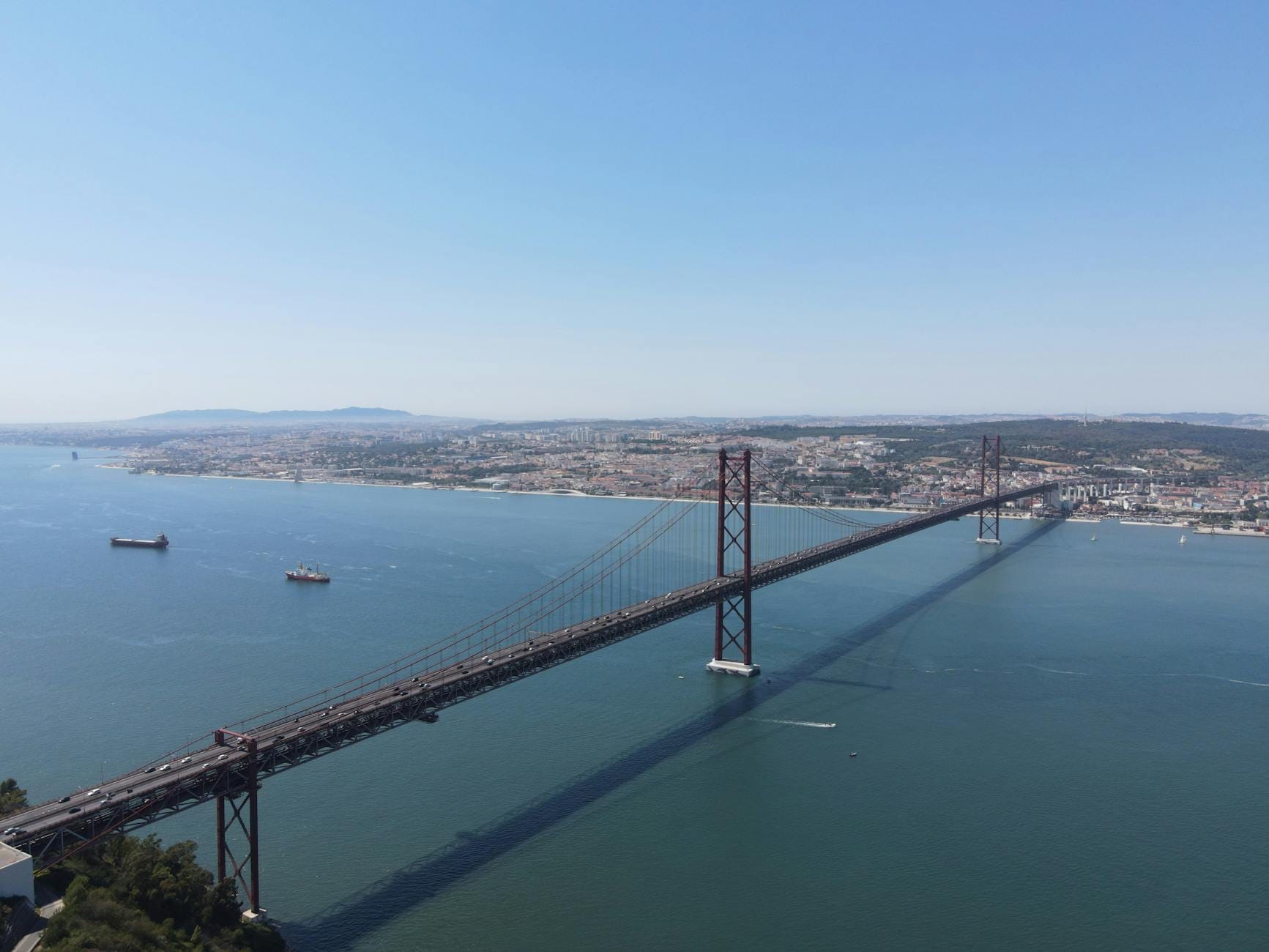 Large vue aérienne du pont 25 de Abril de Lisbonne enjambant le Tage avec la ville en arrière-plan et un ciel dégagé.