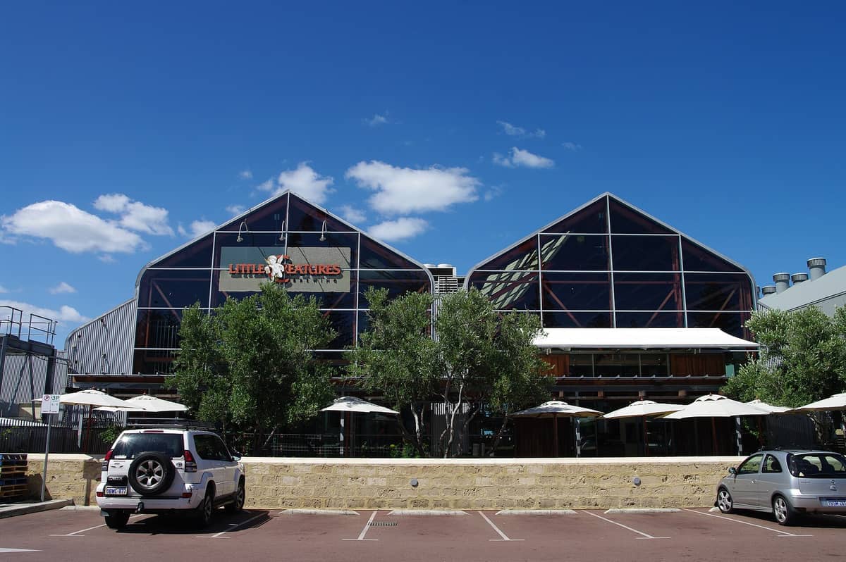 Vorderansicht der Little Creatures Brewery Fremantle mit Glasfassade, Bäumen, geparkten Autos und blauem Himmel über der ikonischen Craft-Beer-Location.