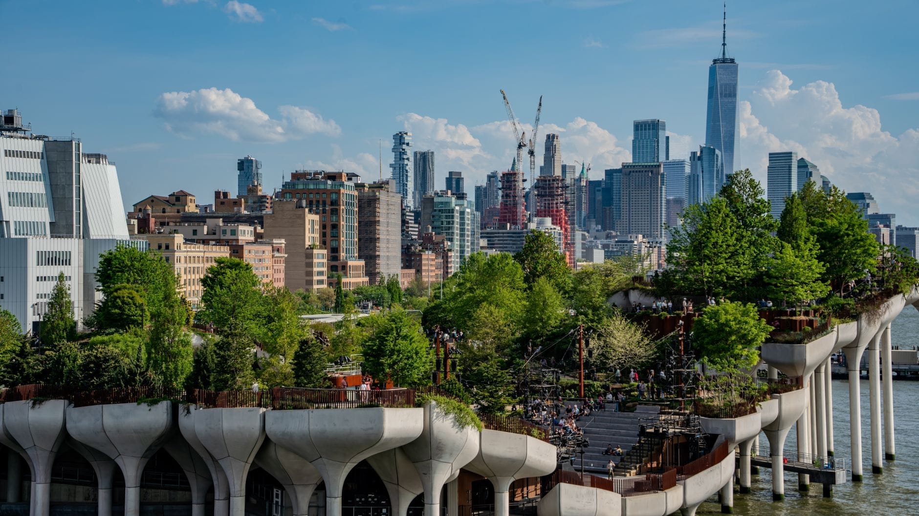 Vista aerea di Little Island al Pier 55, con i piloni in cemento a forma di tulipano, la vegetazione rigogliosa, i visitatori e lo skyline di Manhattan sullo sfondo.