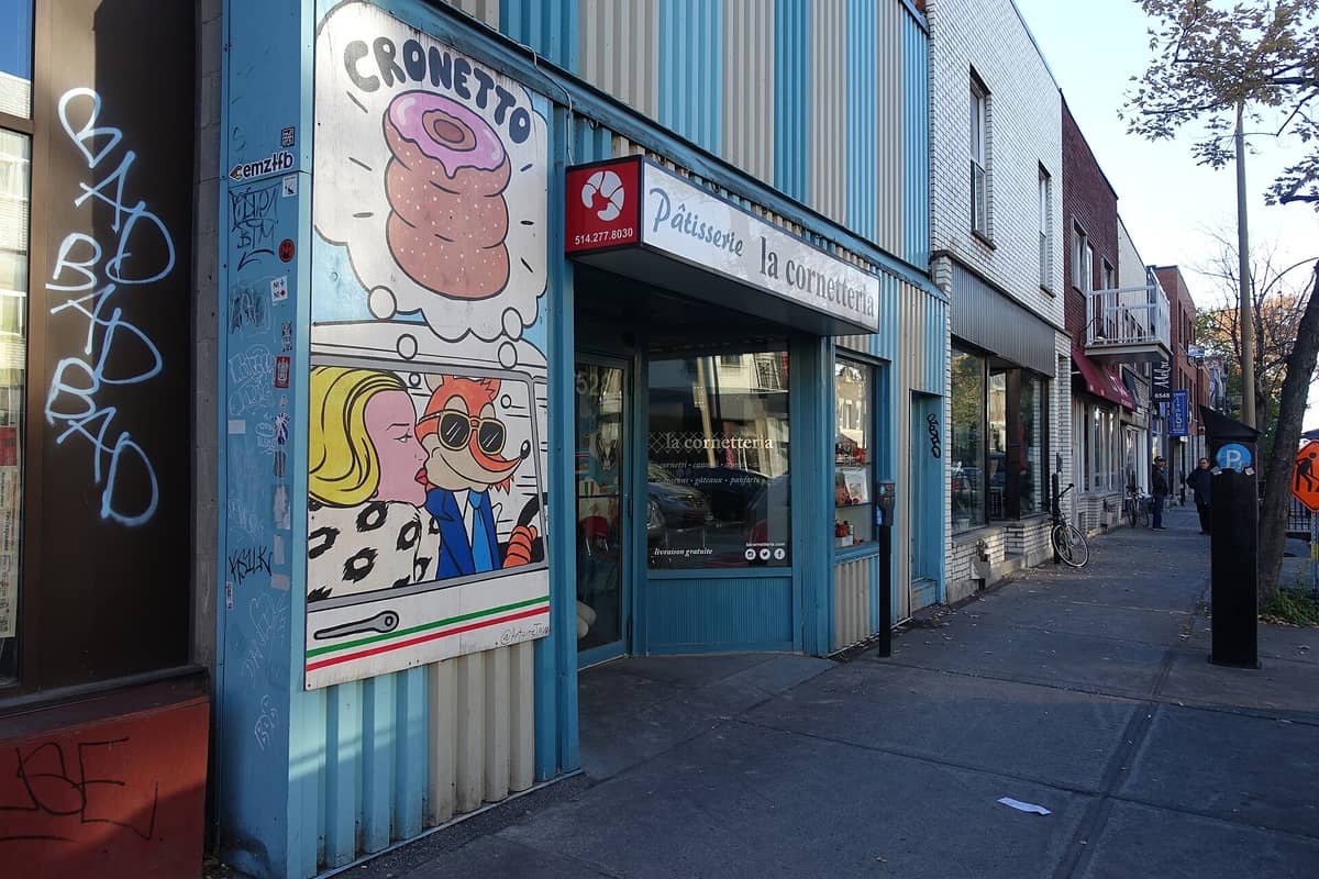 Straßenansicht der Pâtisserie La Cornetteria, einer Konditorei in Montreals Little Italy, mit bunter Fassade und vorbeilaufenden Menschen.
