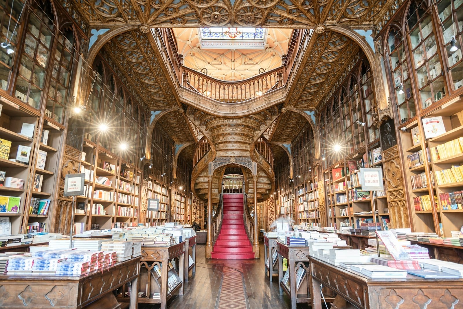 Interno della Livraria Lello con alte librerie, un intricato soffitto in legno e la celebre scalinata rossa immersa nella luce naturale. Un'atmosfera accogliente e maestosa.