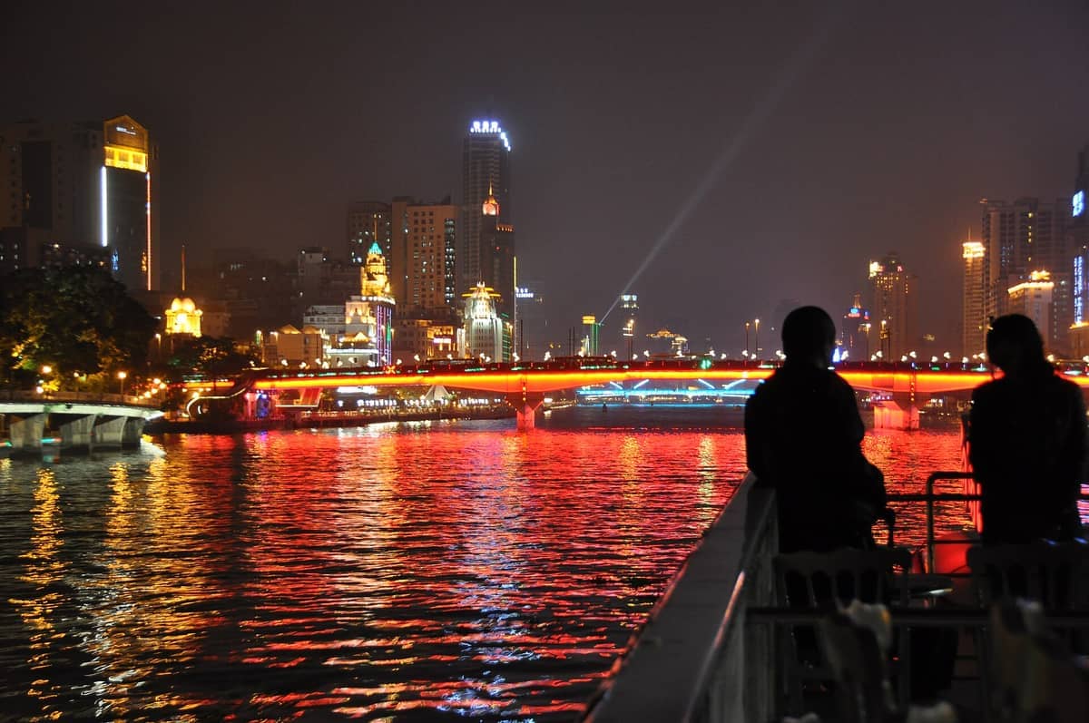 Night view of Liwan District in Guangzhou with illuminated buildings, a brightly lit bridge, and reflections on the Pearl River.