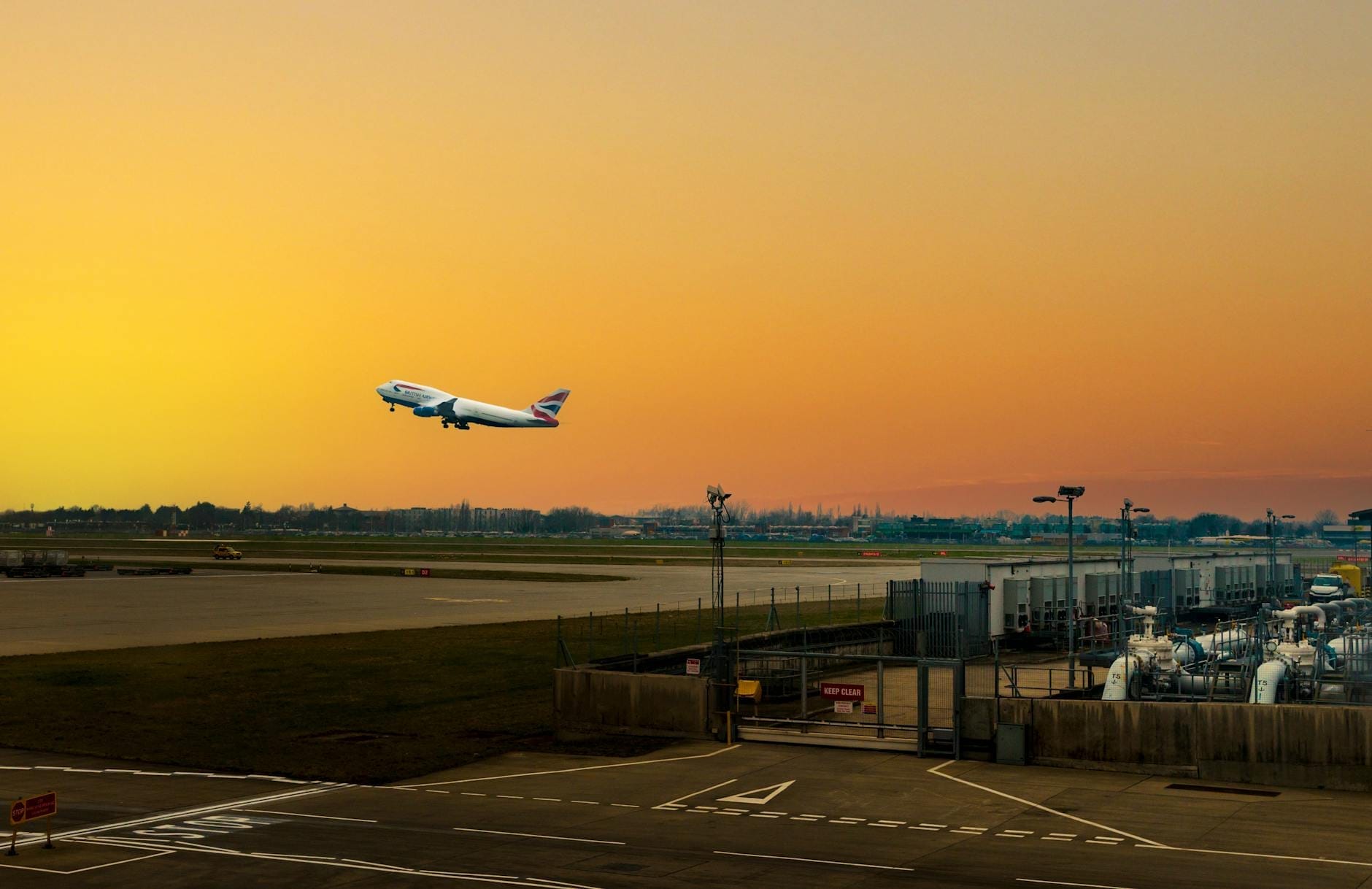 Um avião da British Airways decolando de um aeroporto de Londres ao pôr do sol, com a infraestrutura aeroportuária e uma vista ampla da pista e do céu.
