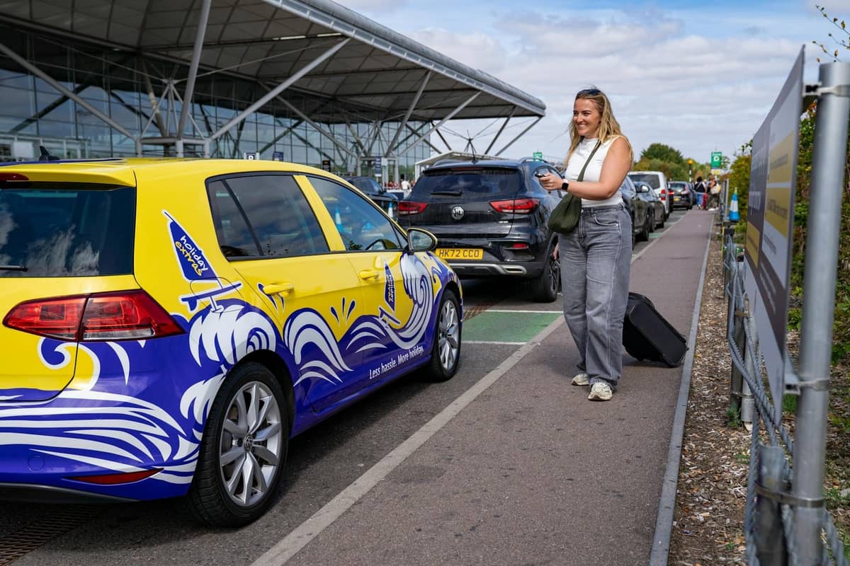 Uma pessoa com uma mala está do lado de fora de um terminal de aeroporto moderno ao lado de um táxi colorido, sugerindo transporte terrestre no aeroporto.