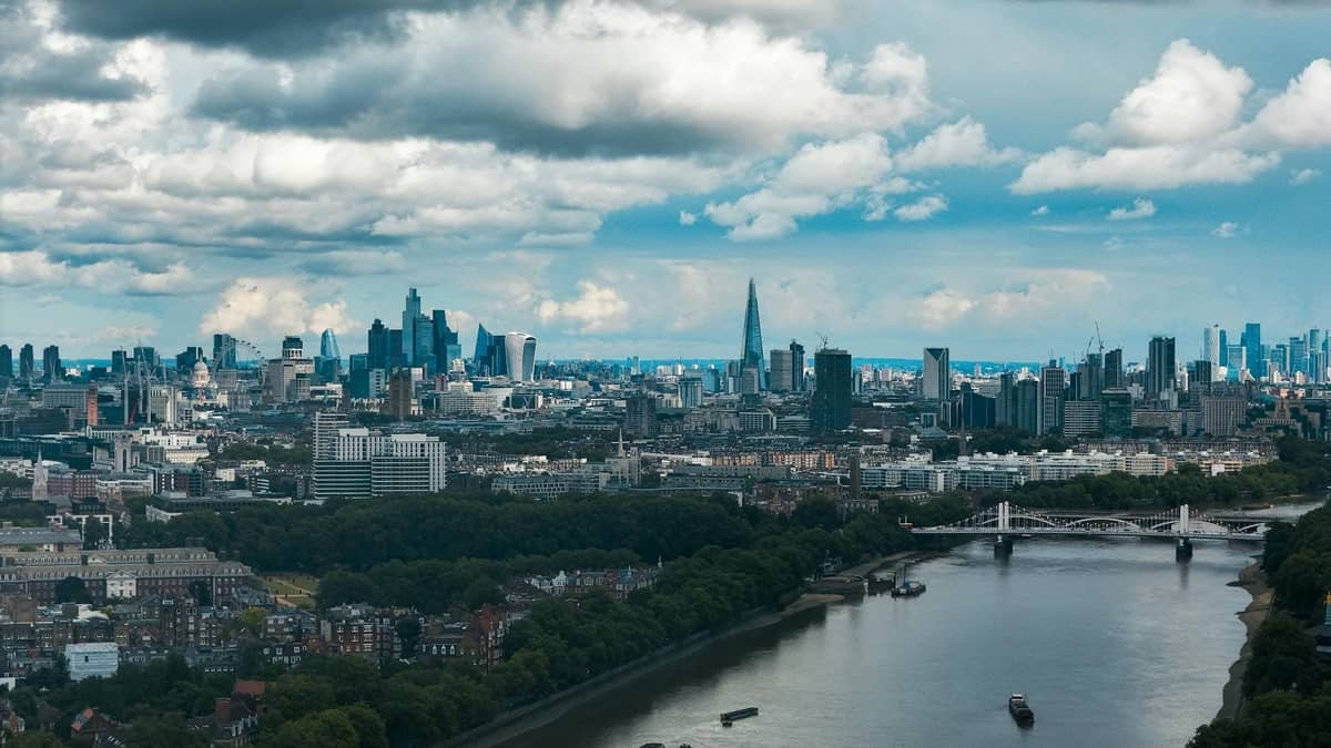 Uma ampla vista aérea diurna do centro de Londres com o rio Tâmisa, o horizonte da cidade e arranha-céus notáveis sob um céu parcialmente nublado.