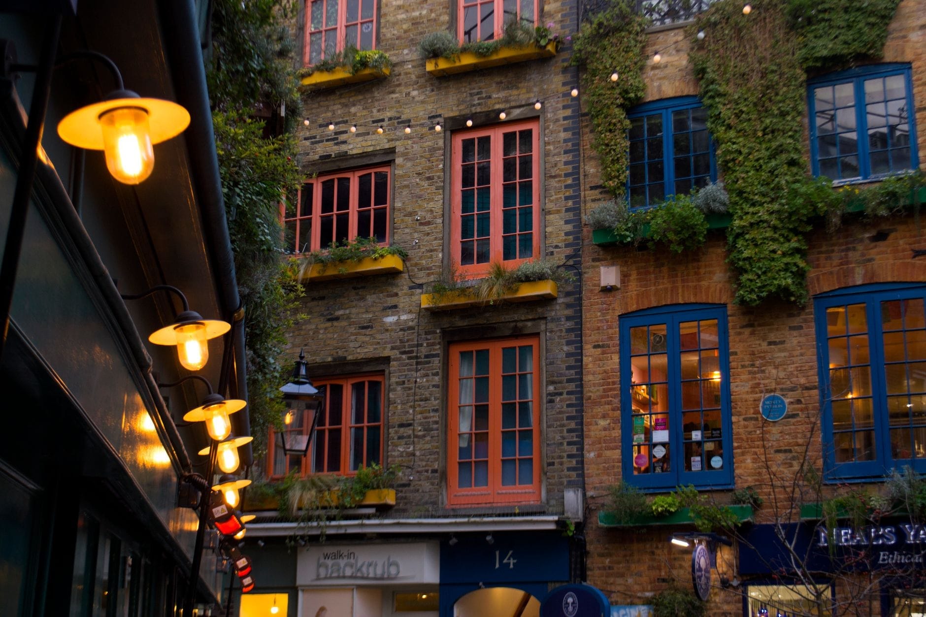 Janelas coloridas e plantas em um pátio escondido de Londres, com luzes pisca-pisca e uma atmosfera charmosa e acolhedora que sugere um ponto favorito dos moradores locais.