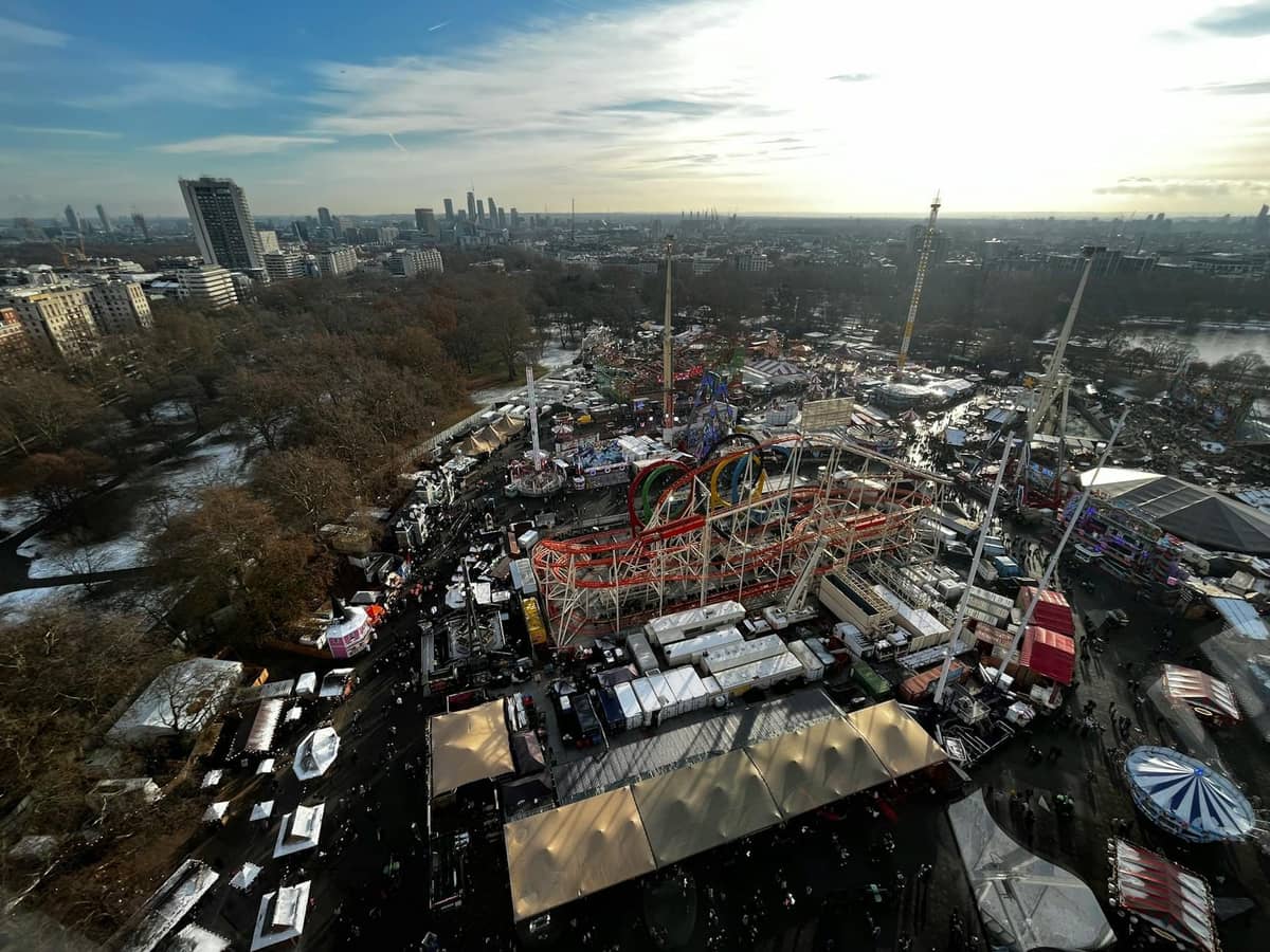 Vista aérea do Hyde Park Winter Wonderland em Londres com brinquedos, montanhas-russas, barracas festivas e multidões, com o horizonte da cidade ao fundo.