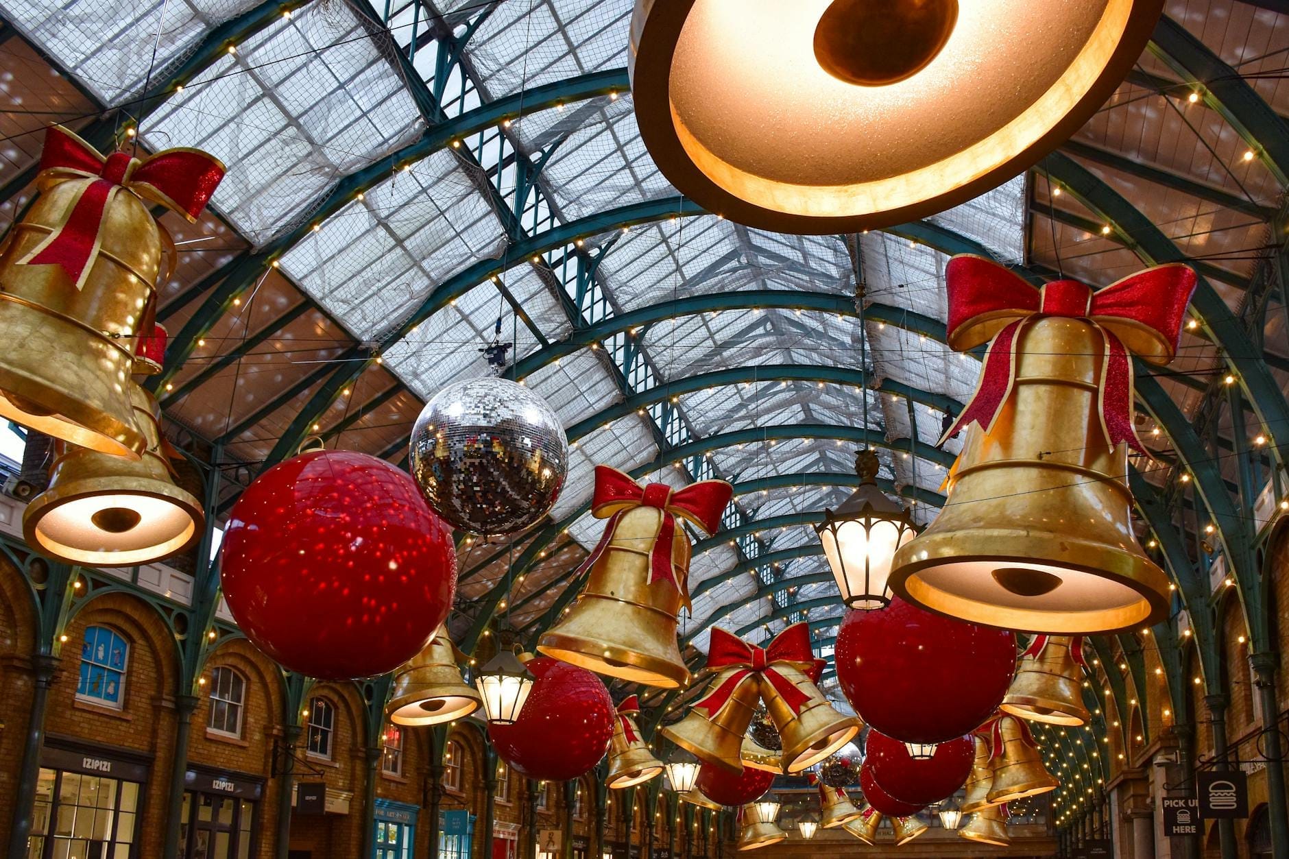 Covent Garden decorado com grandes sinos dourados, bolas vermelhas e luzes de Natal brilhantes sob o teto de vidro, capturando o clima festivo de Londres em dezembro.