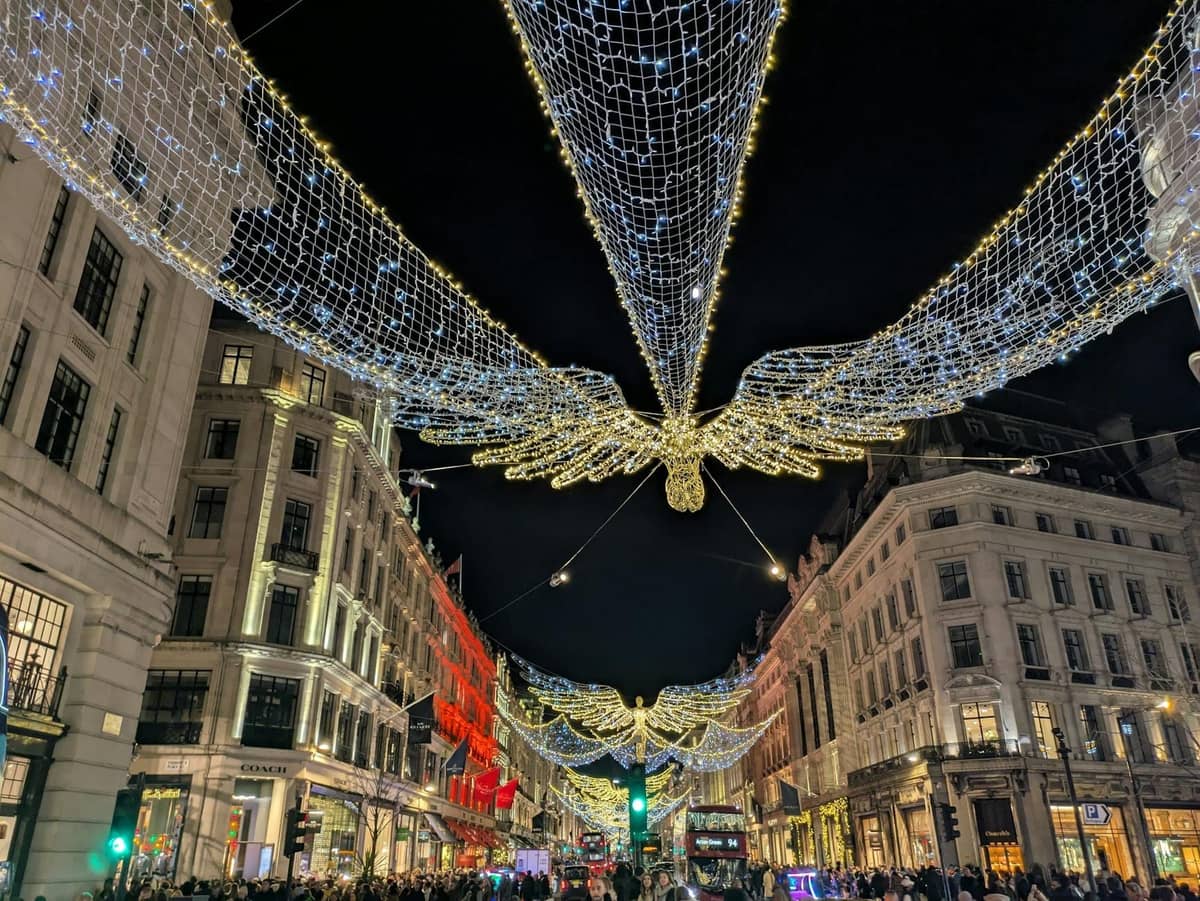 Multidões admiram as luzes natalinas cintilantes em forma de anjo suspensas sobre uma movimentada rua no centro de Londres à noite.