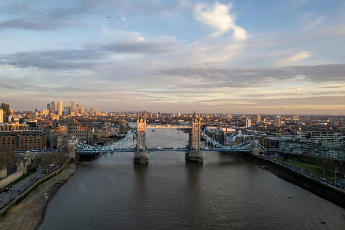 Vista aérea da Tower Bridge sobre o Tâmisa em Londres ao nascer do sol, com o skyline da City ao fundo.