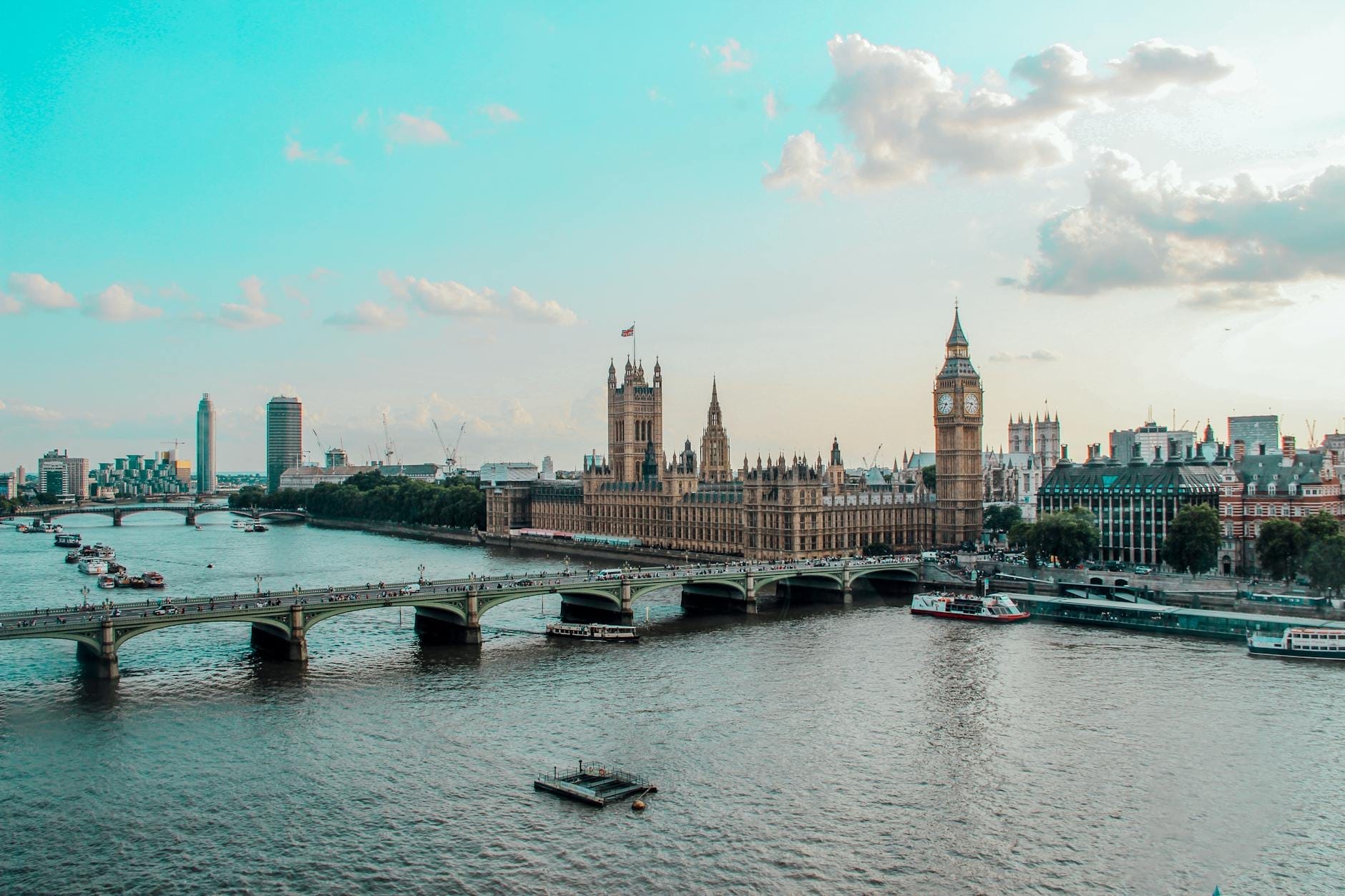 Vista panorâmica do Rio Tâmisa com a Westminster Bridge, o Parlamento e o Big Ben sob um céu azul com algumas nuvens.