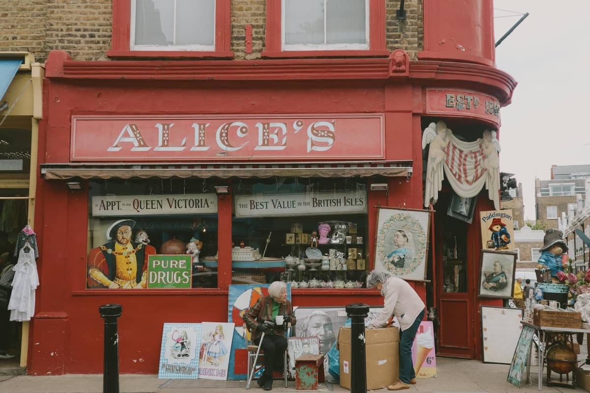 Fachada pintada de vermelho da loja de antiguidades Alice's em Londres com itens vintage e pessoas a ver as peças lá fora.
