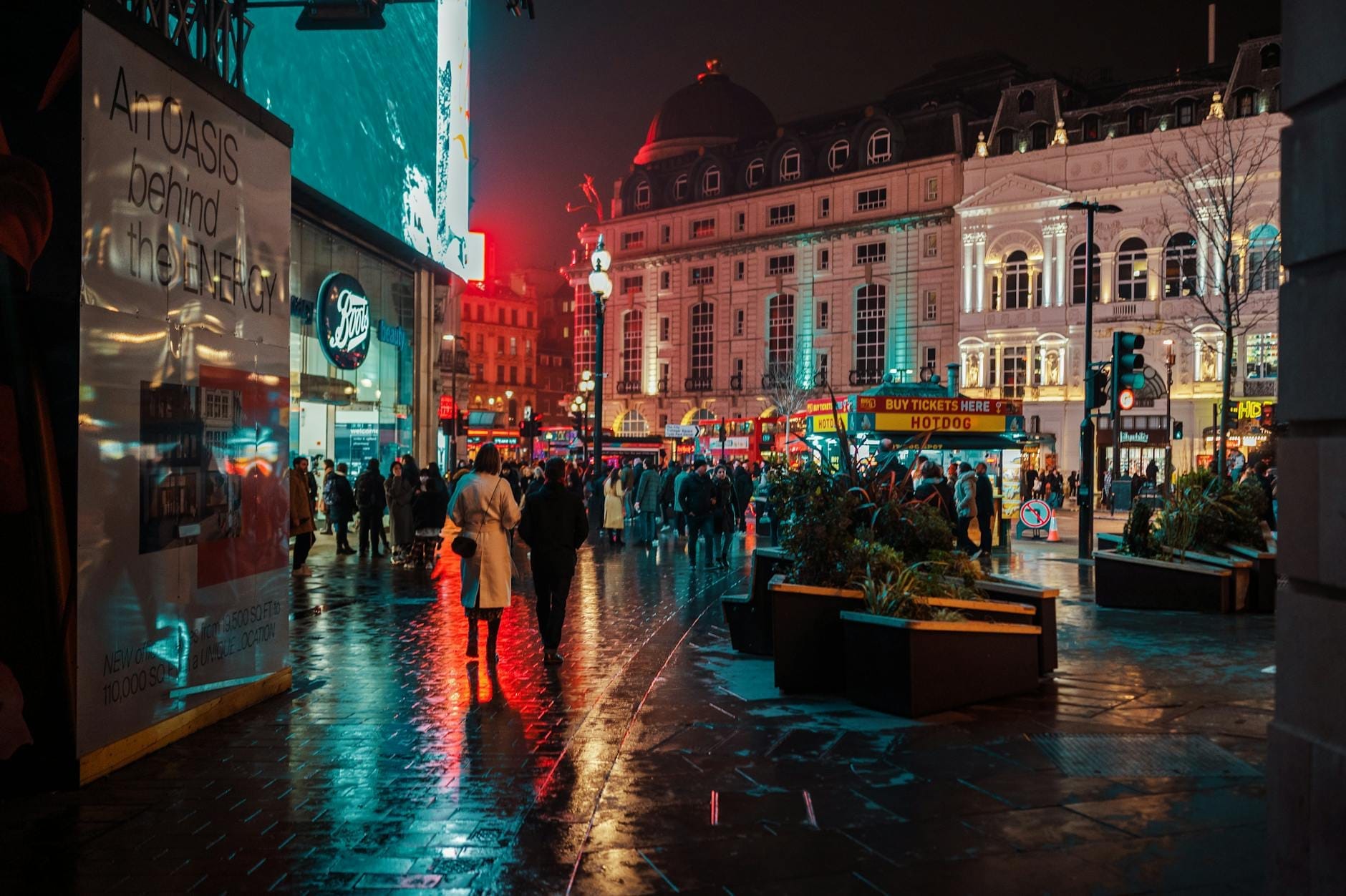 Rua movimentada à noite no centro de Londres com multidões, luzes neon e reflexos, capturando a vibrante atmosfera noturna da cidade.