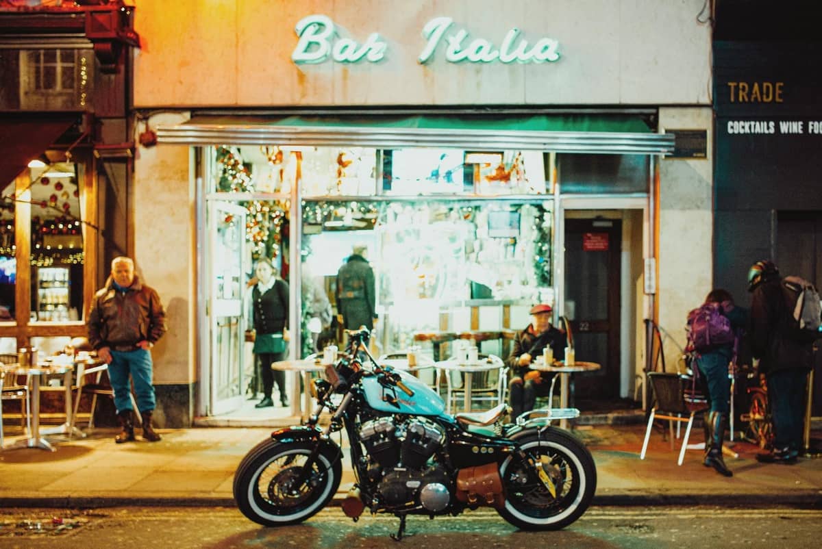 Vista da rua do Bar Italia em Londres à noite com pessoas sentadas do lado de fora e uma motocicleta estacionada na frente.