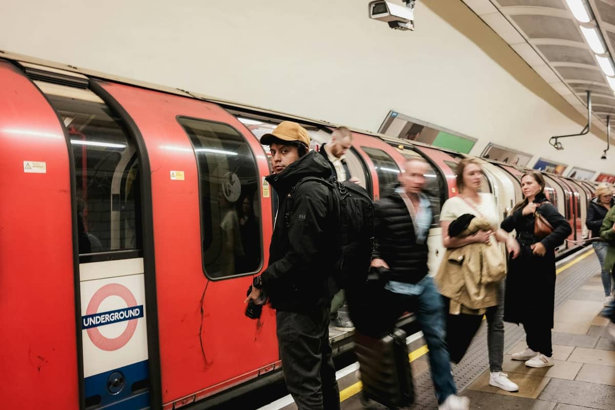Passageiros embarcando em um trem do London Underground na plataforma de uma estação, com o icônico roundel claramente visível.