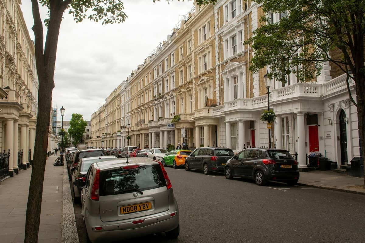 Rua em Londres com fileiras de casas geminadas clássicas, carros estacionados e árvores, opções de alojamento típicas para os visitantes.