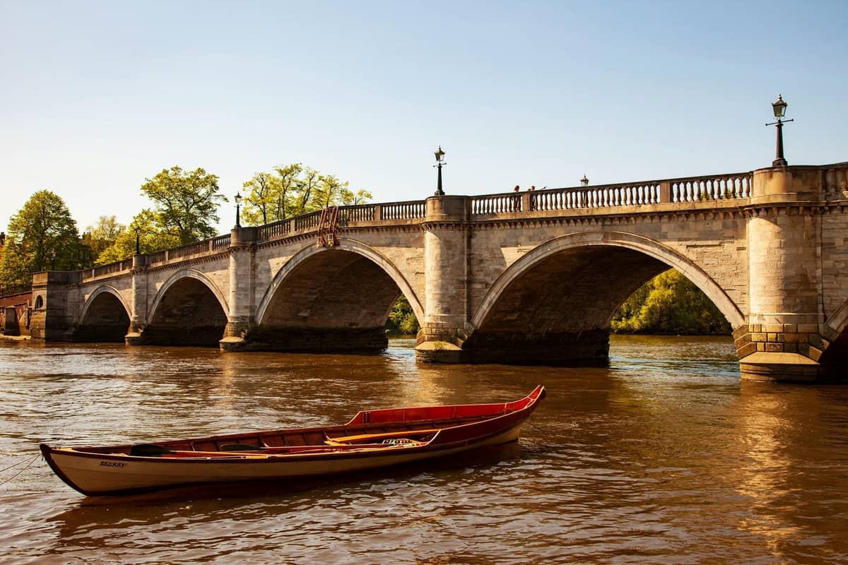 Um barco a remos de madeira no rio Tâmisa perto de uma ponte de pedra em Londres sob céus limpos.