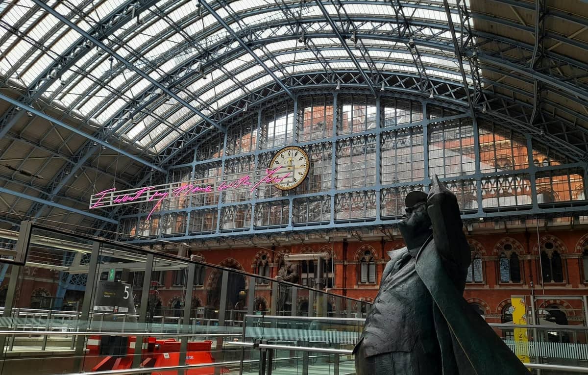 Interior da estação London St Pancras International com o icónico relógio, teto de vidro e estátua visíveis.