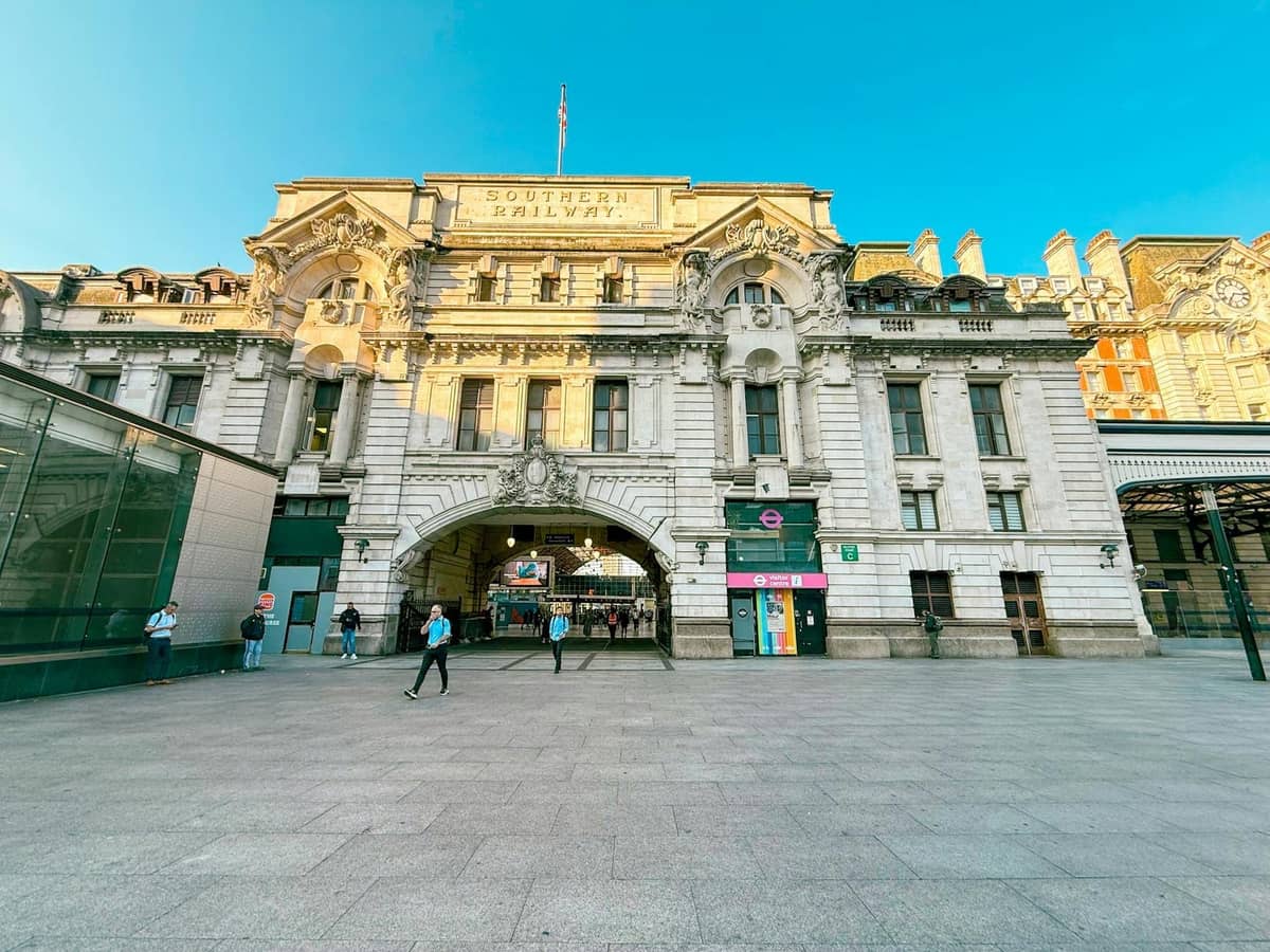 Fachada e entrada da London Victoria Coach Station com pessoas caminhando na frente em um dia ensolarado