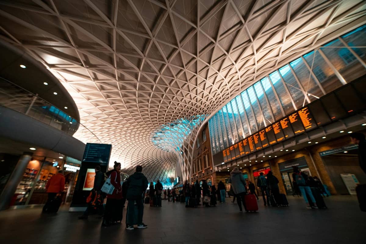 Interior da estação London King's Cross, viajantes sob um intrincado teto moderno com um grande painel de partidas visível acima.