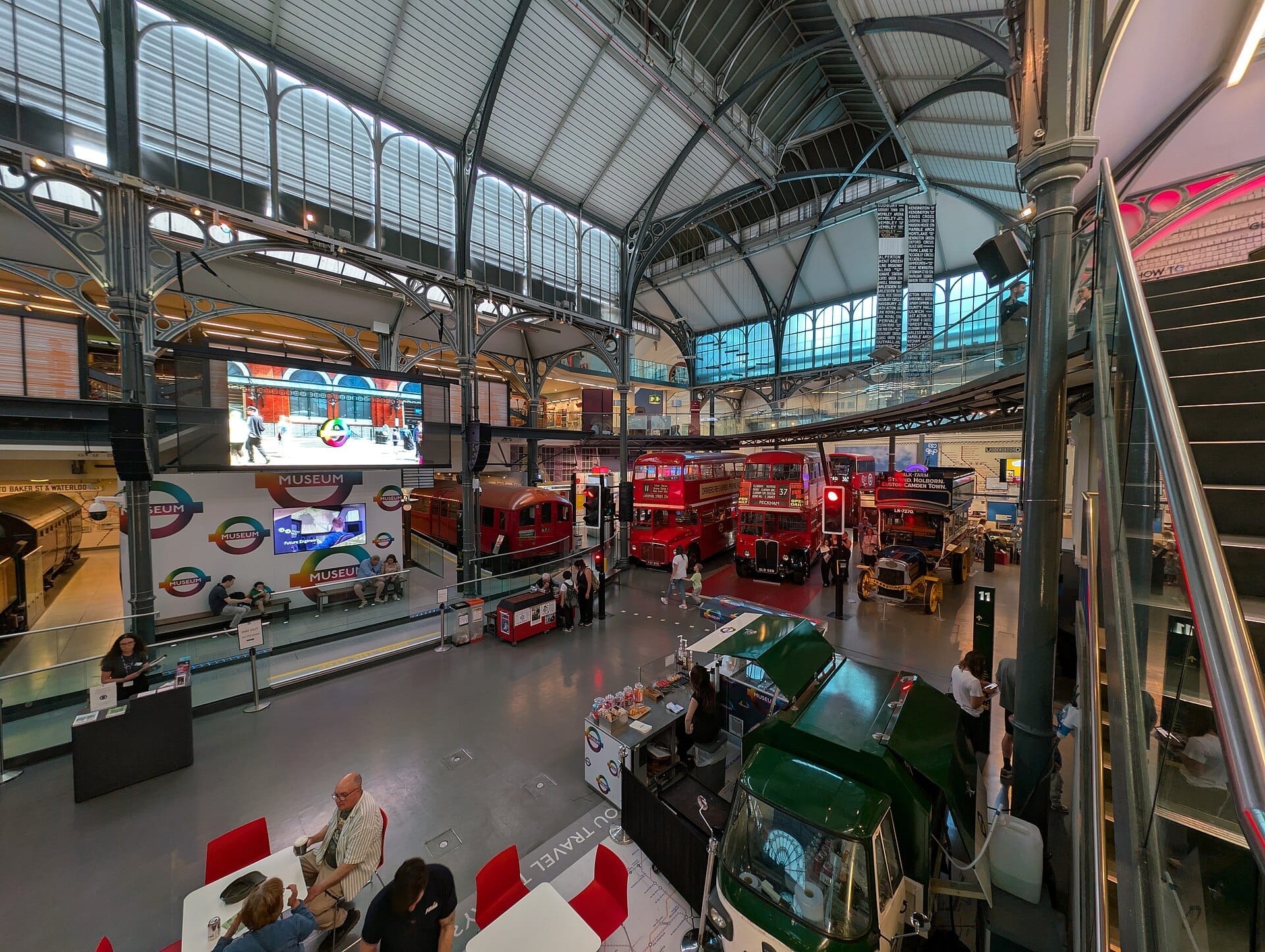 Vista interna del London Transport Museum con autobus rossi d'epoca, una carrozza della metropolitana storica e ferro battuto vittoriano sotto un soffitto in vetro.