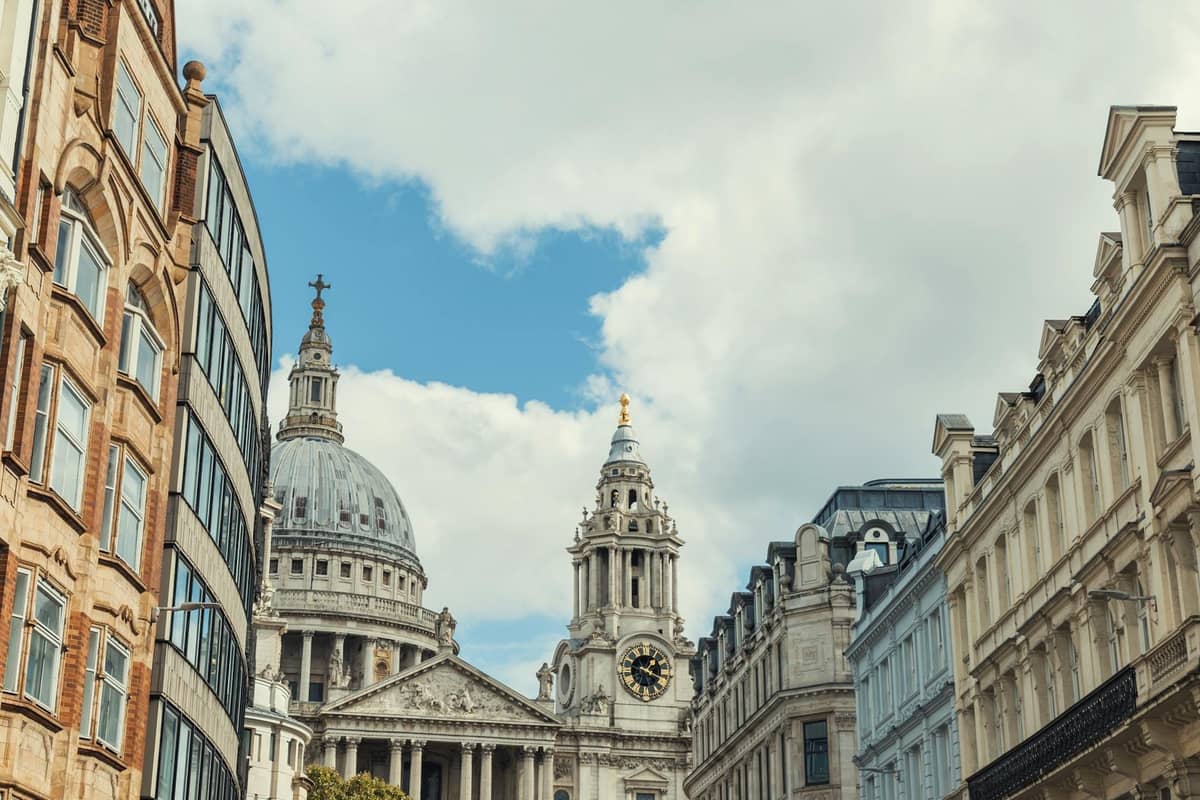 Vista ao nível da rua da Catedral de St Paul rodeada de edifícios históricos sob um céu azul na City de Londres.