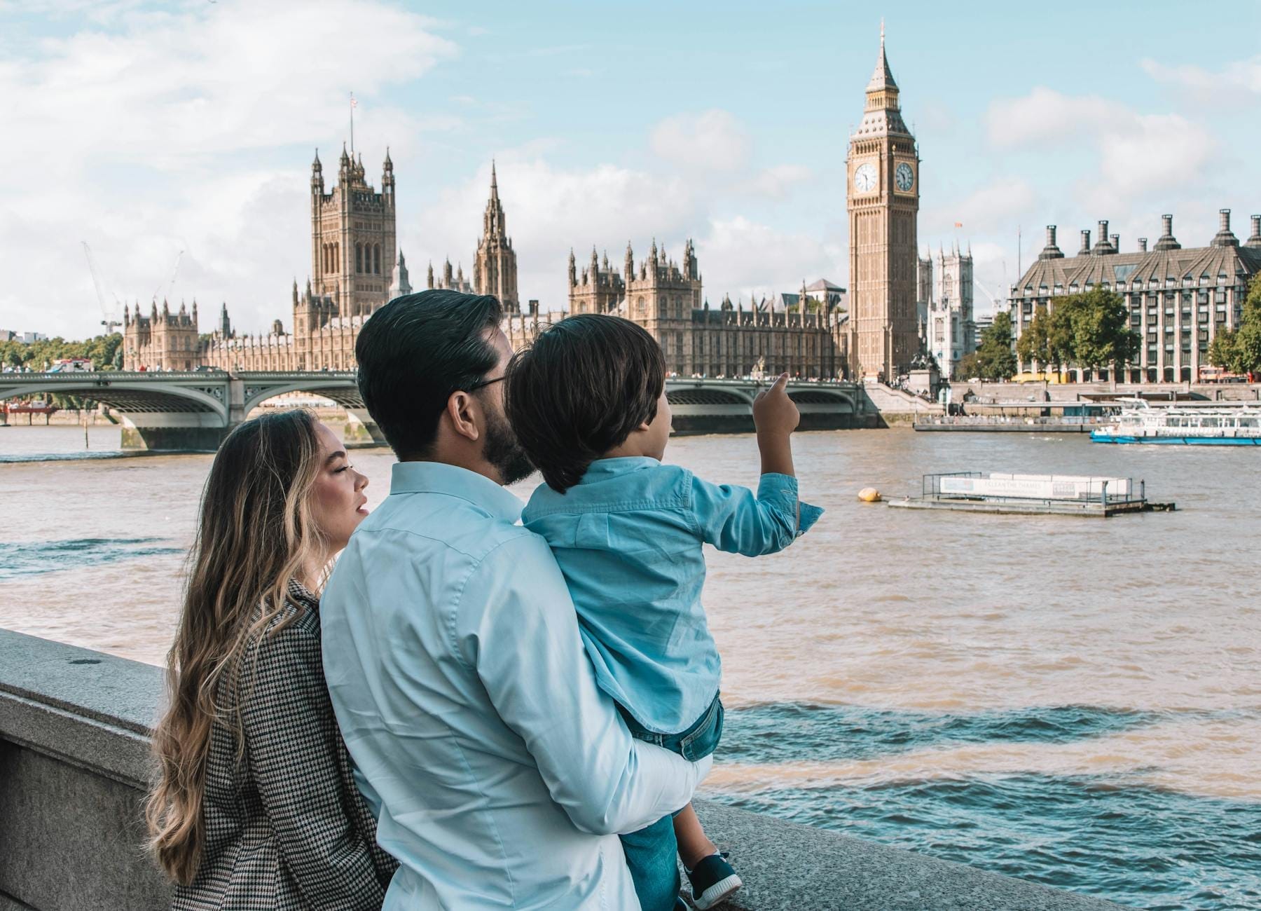 Família com criança pequena contemplando o Tâmisa em direção ao Big Ben e ao Parlamento em um dia ensolarado em Londres.