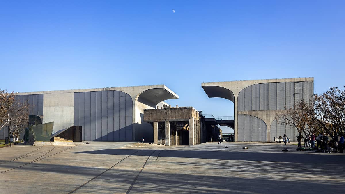 Weitwinkelaufnahme der markanten Beton-Stahl-Fassade des Long Museum West Bund mit einem Vorplatz und Besuchern unter einem strahlend blauen Shanghaianer Himmel.