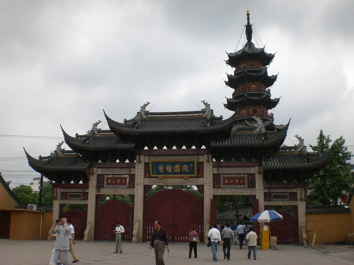 Eingangstor und historische mehrstöckige Pagode des Longhua-Tempels in Shanghai, mit Besuchern, die unter bewölktem Himmel spazieren.