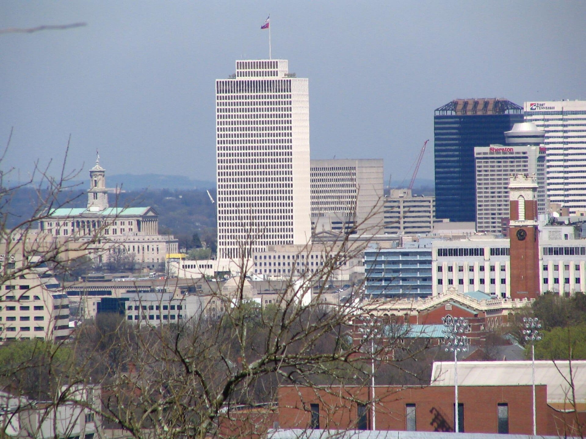 Horizonte del centro de Nashville visto desde Love Circle, con altos edificios de oficinas, el State Capitol, una torre con reloj y ramas de árboles en primer plano.