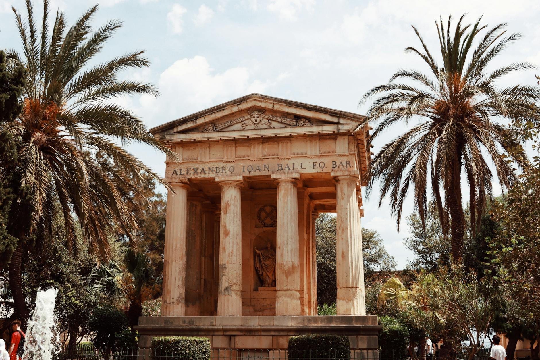 Il monumento neoclassico a Sir Alexander Ball incorniciato da palme nei Giardini della Barrakka Inferiore, Valletta, in una giornata luminosa.