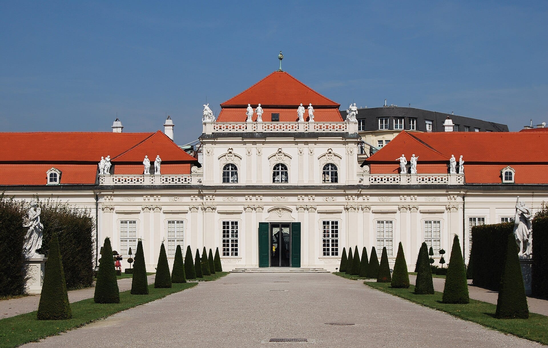 Frontansicht des Unteren Belvedere in Wien mit symmetrischer Barockarchitektur, rotem Dach, Statuen und gepflegten Gärten unter einem klaren blauen Himmel.