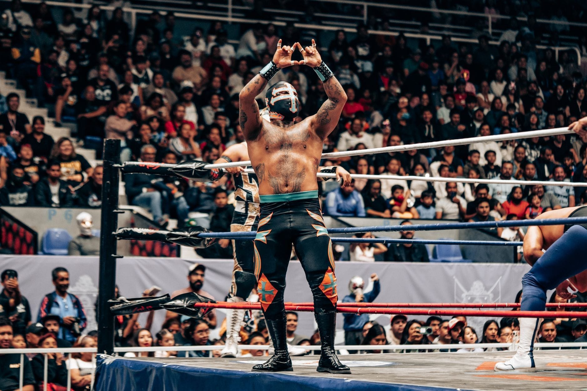 Um luchador mascarado fica sobre as cordas do ringue, gesticulando para uma multidão animada em uma arena de lucha libre lotada.