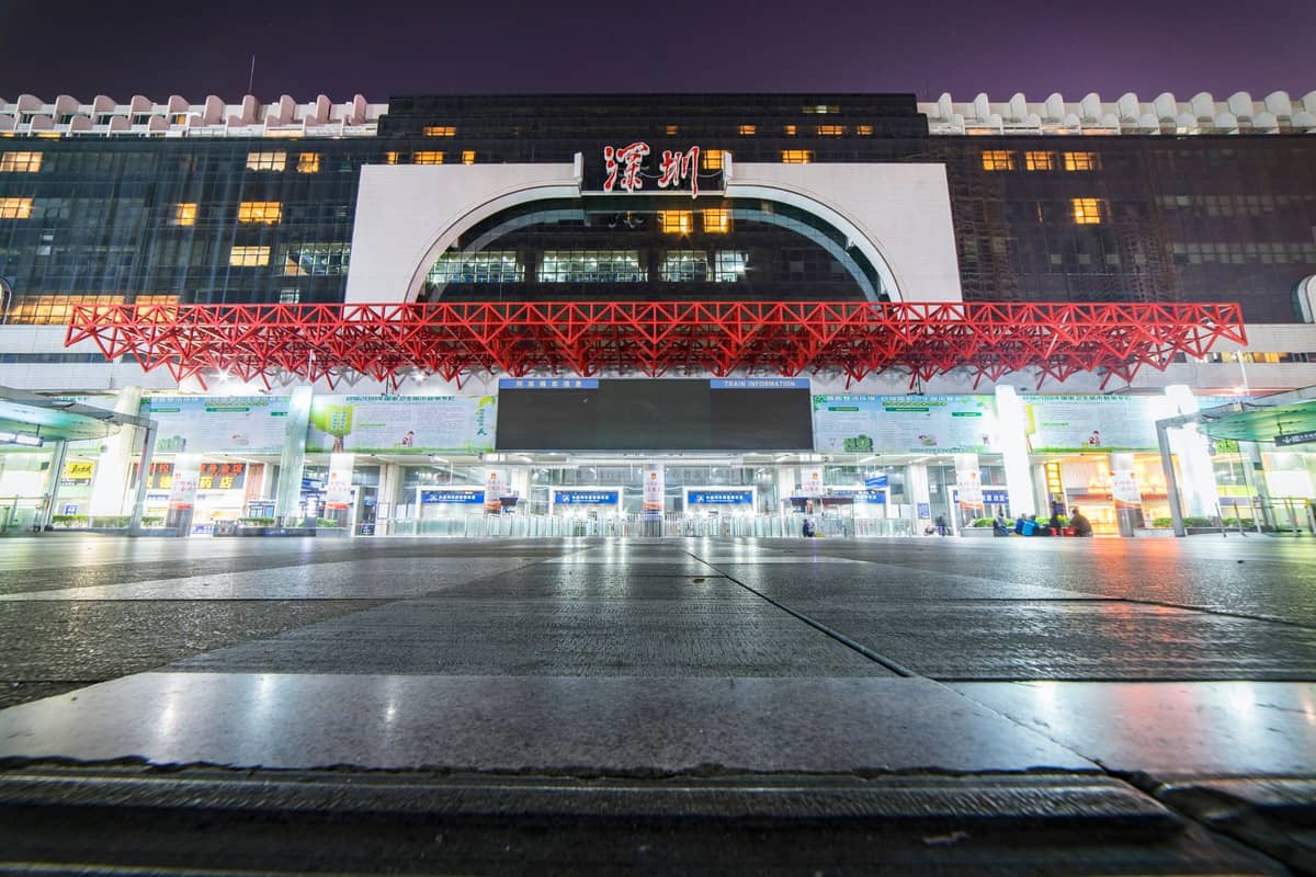 Vista noturna da entrada principal da Estação Ferroviária de Shenzhen em Luohu, com luzes brilhantes, arquitetura moderna e cobertura vermelha característica.