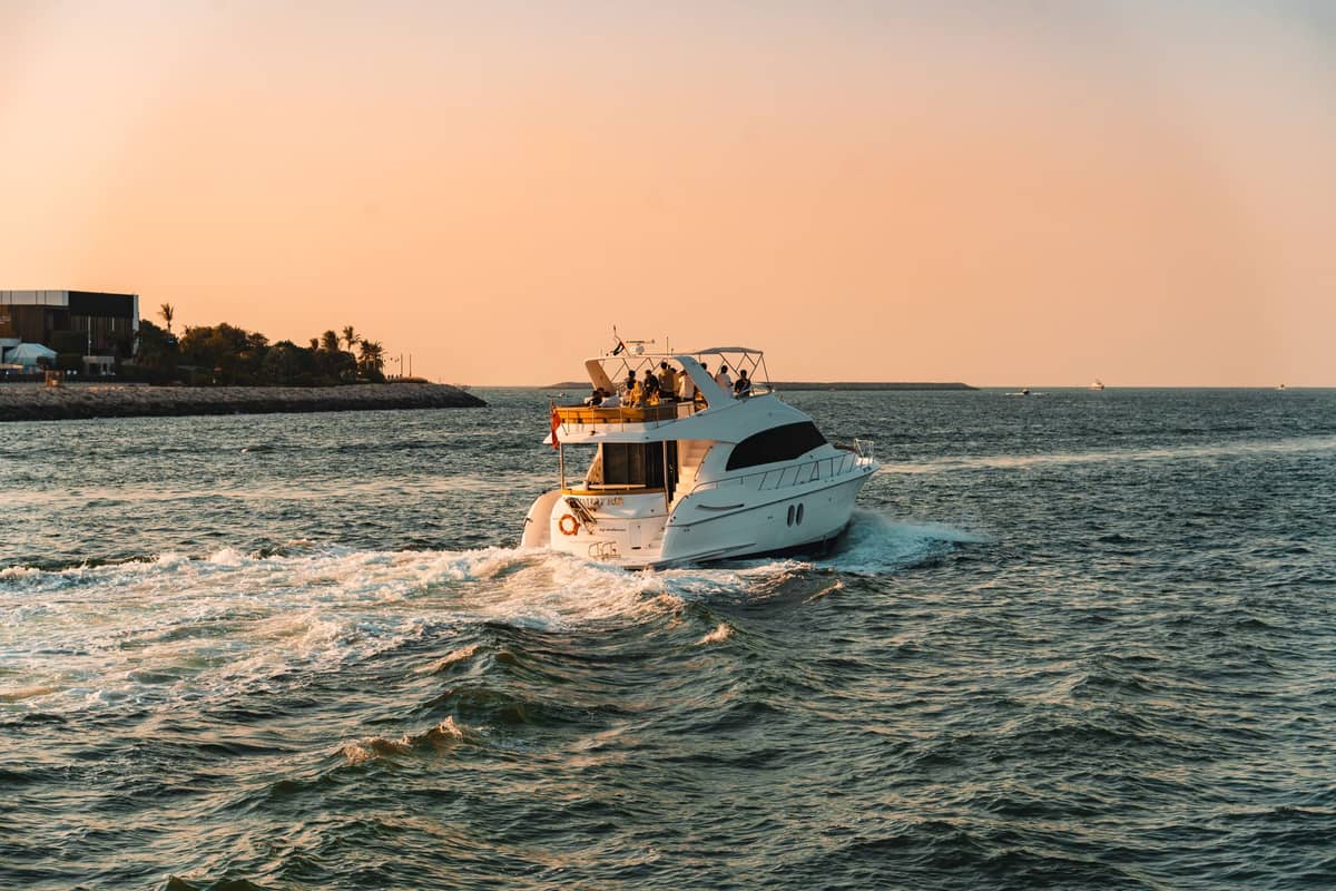 Luxury yacht cruising away from Cartagena’s coastline at sunset, with people on board and city structures visible on the horizon.