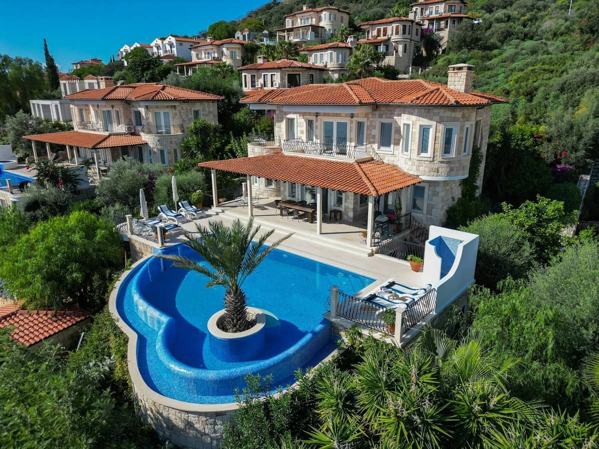 Vista aerea di una lussuosa villa in pietra con piscina a sfioro privata circondata da rigogliosa vegetazione e altre ville di lusso su una collina