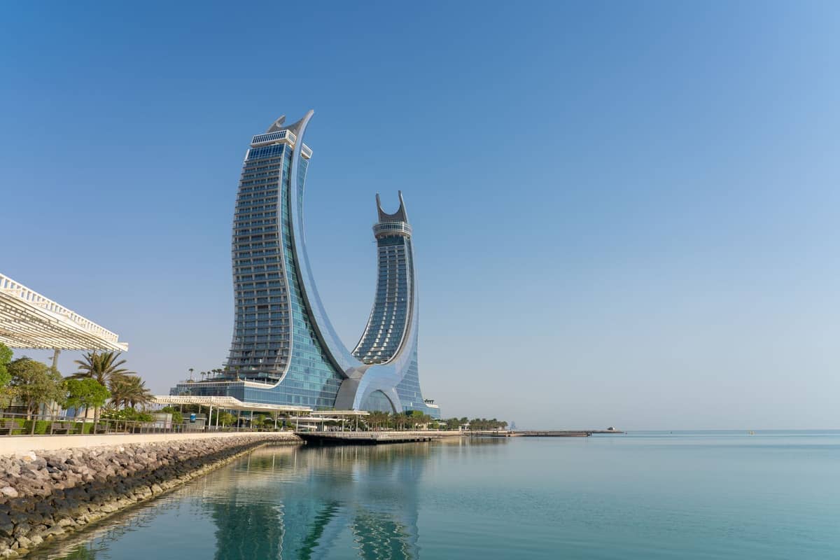 Die ikonischen geschwungenen Türme des Hotelkomplexes Katara Towers spiegeln sich im ruhigen Meer unter klarem blauem Himmel in Doha, Katar.