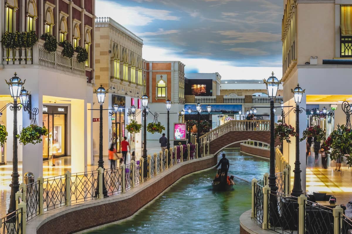 Überdachter Kanal und Gondel umgeben von gehobenen Geschäften im Villaggio Mall in Doha, mit Gewölbedecke und dekorativen Straßenlaternen.