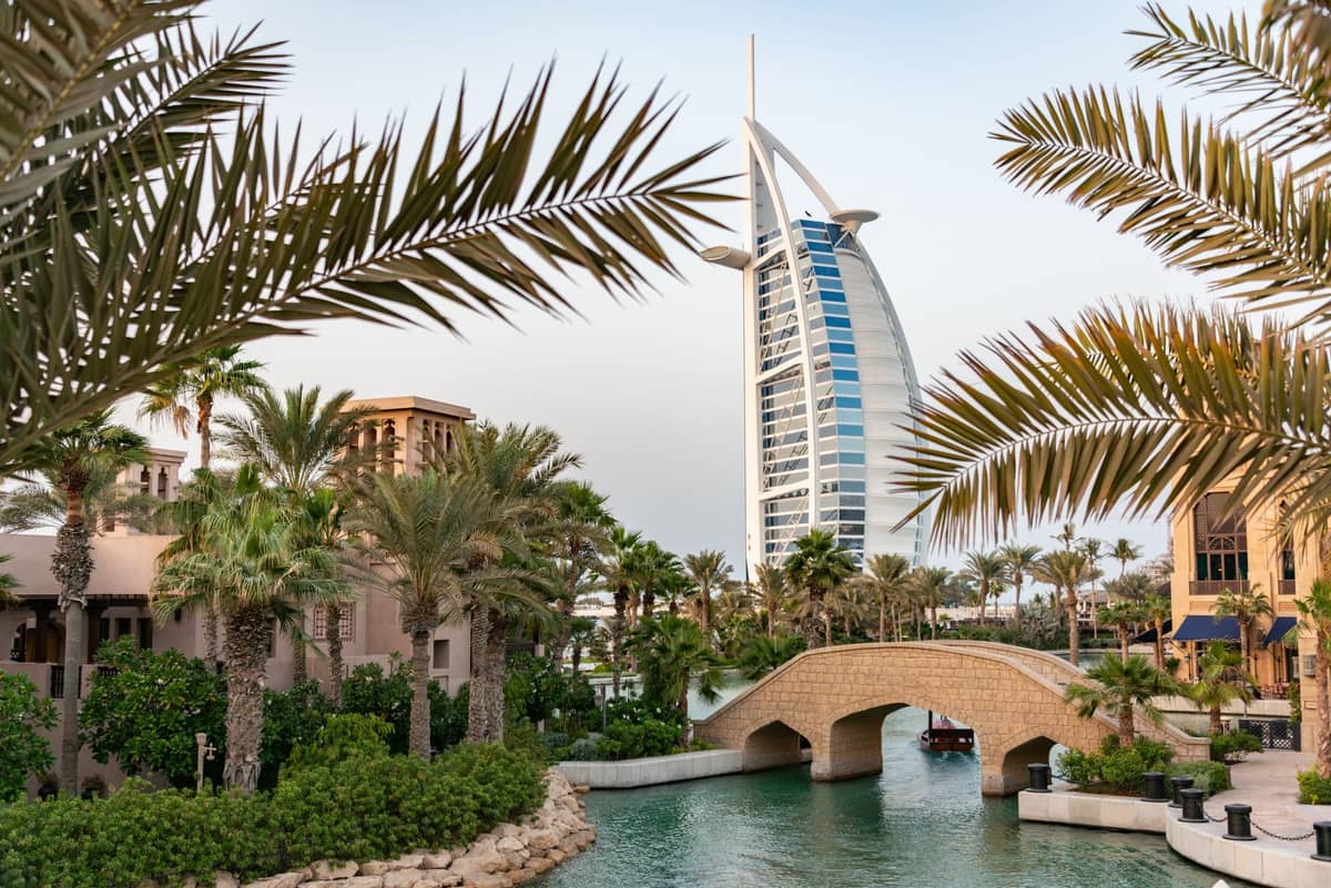 Blick auf die Luxushotels Burj Al Arab und Madinat Jumeirah in Dubai, mit Palmen, Kanal und Bogenbrücke im Vordergrund.
