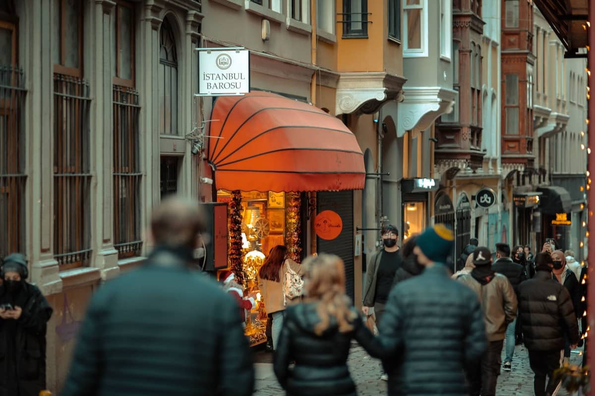 Multitud caminando frente a tiendas exclusivas en una elegante y estrecha calle de Estambul con arquitectura elegante y cálidas luces.