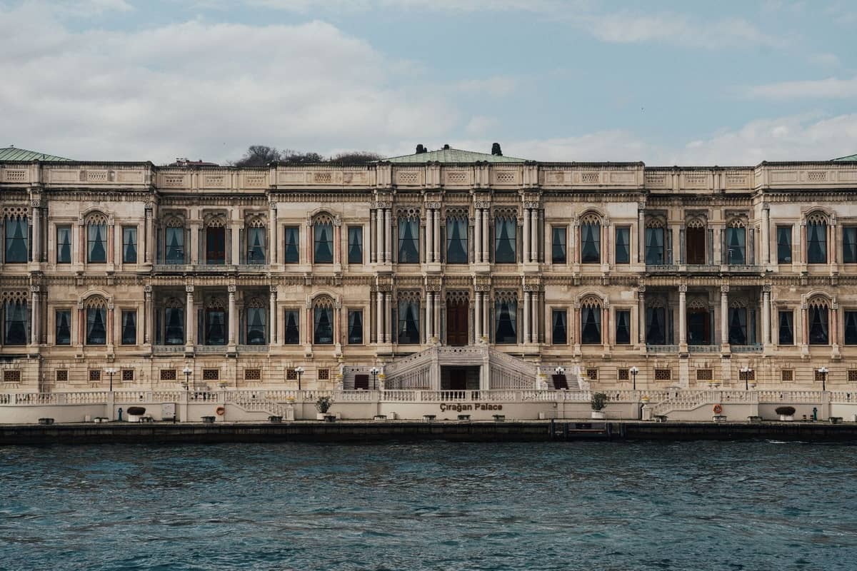 Gran hotel palacio histórico frente al mar con fachada ornamentada, grandes ventanas y escalinatas directamente junto al estrecho del Bósforo en Estambul.