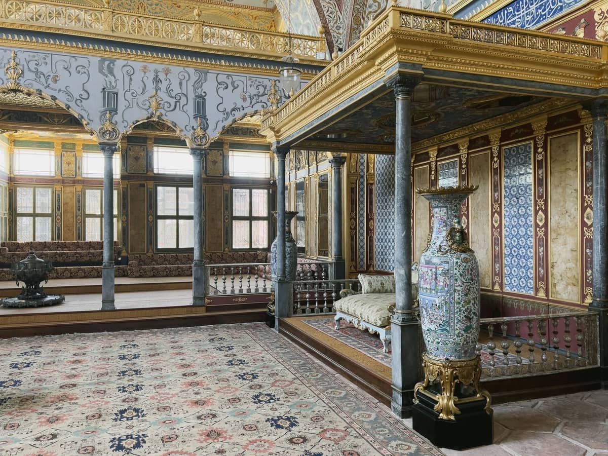 Cámara interior lujosamente decorada del Palacio Topkapi con muebles ornamentados, alfombras con estampados, detalles dorados y grandes jarrones decorativos