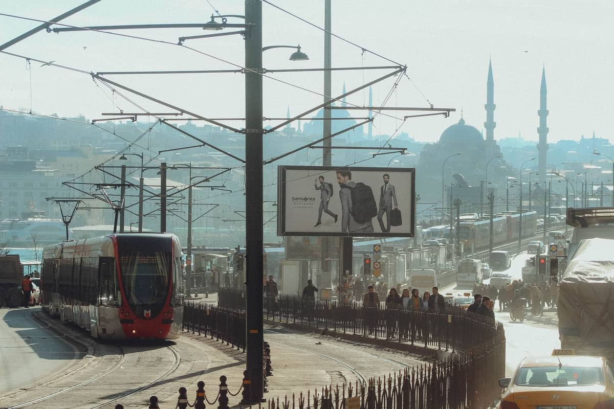 Tranvía moderno cruzando el Puente de Gálata en Estambul con mezquitas históricas y el horizonte de la ciudad al fondo, escena urbana diurna.