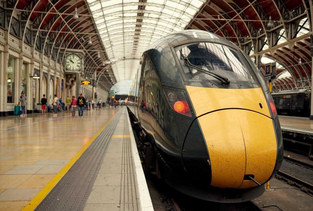 Trem moderno de alta velocidade na plataforma da estação London Paddington com teto arqueado e passageiros próximos.
