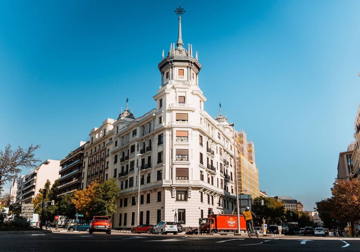 Elegante edificio en esquina con torre redondeada y arquitectura clásica, situado en una amplia calle madrileña soleada con un entorno exclusivo.