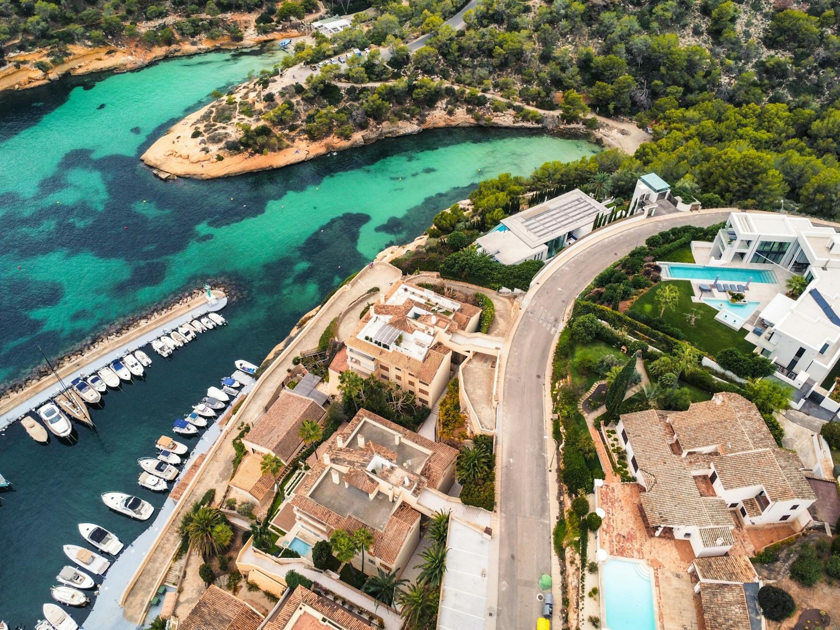Vista aérea de vilas de luxo, hotéis sofisticados, marina turquesa com iates e uma bela costa em Mallorca cercada por vegetação exuberante.